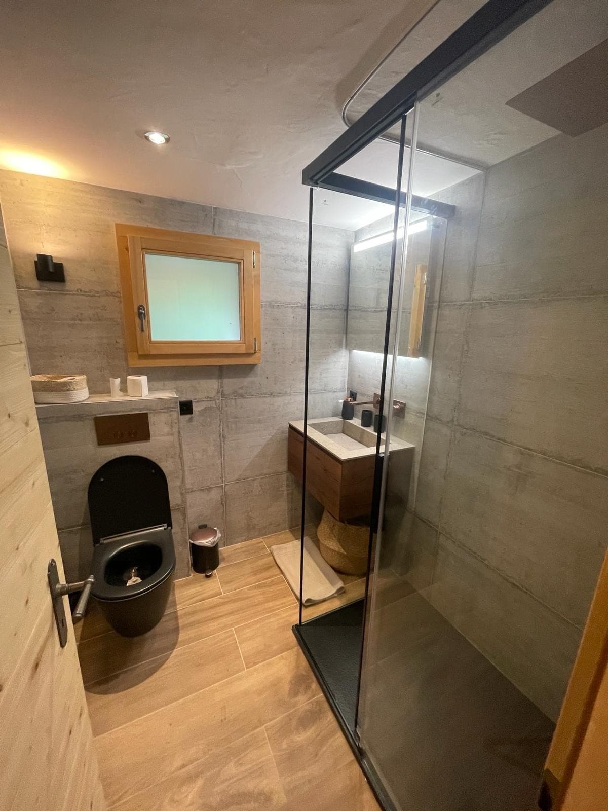 Salle d'eau en bois et carrelage clair avec cabine de douche transparente, réalisation DEN Sanitaire à Verbier
